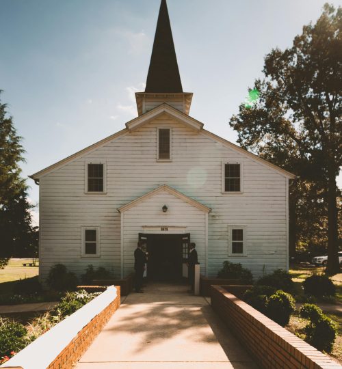 A picturesque chapel with a steeple and wooden architecture set in the countryside under clear skies.